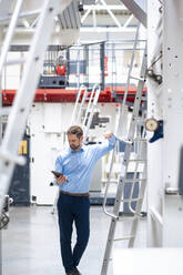 Businessman using tablet PC standing by ladder at industry - JOSEF14275