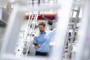 Businessman using tablet PC standing by ladder at industry - JOSEF14276