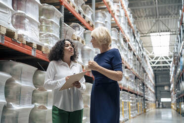 Senior businesswoman discussing with colleague holding clipboard in industry - JOSEF14301