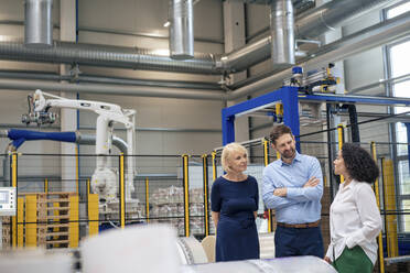 Businesswoman standing with hand in pocket discussing with colleagues at industry - JOSEF14320