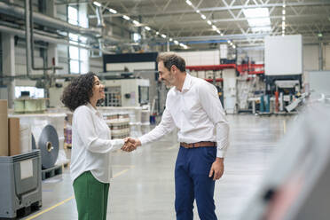 Happy mature businessman shaking hand with businesswoman in industry - JOSEF14329