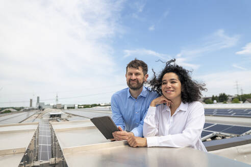 Lächelnde Geschäftsfrau steht neben einem Geschäftsmann, der einen Tablet-PC auf einem Dach hält - JOSEF14335