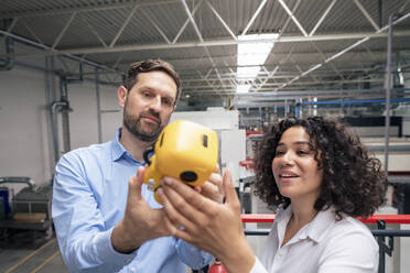 Smiling businesswoman and businessman analyzing mini robot in industry - JOSEF14344