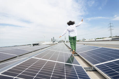 Businesswoman with arms outstretched walking amidst solar panels on rooftop - JOSEF14374