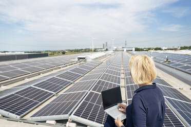 Ältere Geschäftsfrau mit Laptop vor einem Solarpanel - JOSEF14378