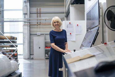 Smiling senior businesswoman standing by computer monitor in industry - JOSEF14379