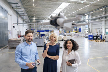 Ältere Geschäftsfrau mit Kollegen, die eine fliegende Drohne in der Industrie analysieren - JOSEF14399