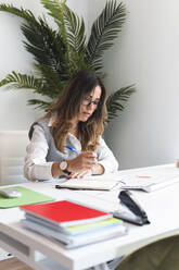 Young lawyer making notes sitting at desk in office - JAQF01049