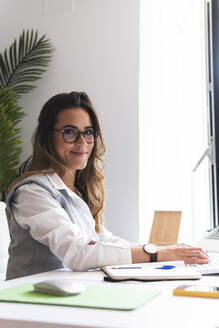 Smiling young lawyer wearing eyeglasses sitting at office desk - JAQF01053