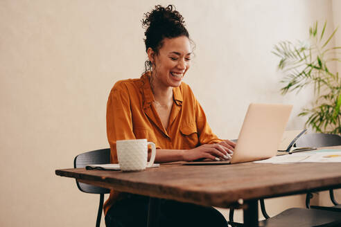 Lächelnde Frau, die zu Hause am Laptop arbeitet. Frau sitzt mit einer Kaffeetasse am Tisch und benutzt einen Laptop. - JLPSF08115