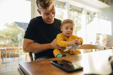 Lächelnder Mann mit seinem Sohn am Tisch sitzend. Vater mit seinem süßen kleinen Jungen zu Hause. - JLPSF08149