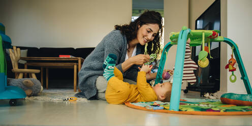 Mother using rattle toys while playing with her baby boy. Woman playing with her new born son at home. - JLPSF08151