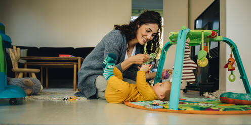 Mutter mit Rassel Spielzeug beim Spielen mit ihrem kleinen Jungen. Frau spielt mit ihrem neu geborenen Sohn zu Hause. - JLPSF08151