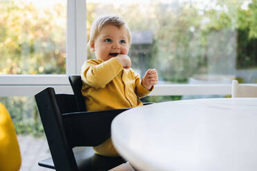 Süßes Baby sitzt auf einem Stuhl am Tisch. Kind wartet auf Essen. Süßes Baby sitzt in einem Hochstuhl und wartet auf das Essen. - JLPSF08157