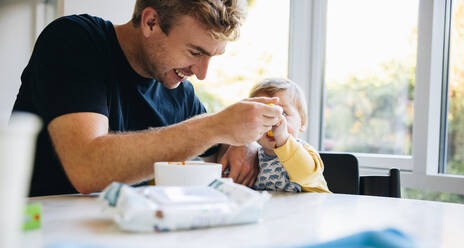 Liebevoller Vater, der sein Baby während des Vaterschaftsurlaubs mit einem Löffel füttert. Mann, der sein kleines Baby während des Vaterschaftsurlaubs mit einem Löffel füttert. - JLPSF08159