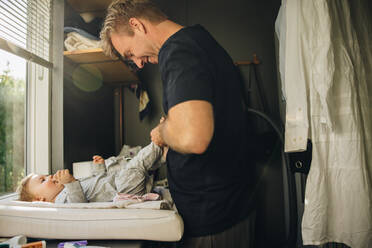 Ein Mann wechselt die Kleidung seines Kleinkindes. Ein Vater wechselt die Windel und die Kleidung seines Babys, während er in Vaterschaftsurlaub ist. - JLPSF08170