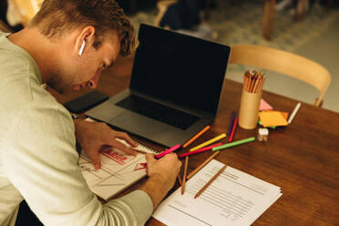 Man working at home drawing designs on a paper with a colored pencil. Male designer preparing illustrations. - JLPSF08195