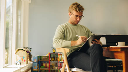 Hardworking man drawing sketches on his tablet computer. Illustrator using graphic tablet for making new designs while sitting in a chair at home. - JLPSF08196