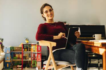 Portrait of a female designer sitting on chair at home with digital tablet. Confident woman with tablet computer at home. - JLPSF08197