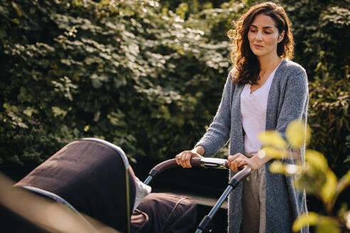 Frau, die einen Kinderwagen schiebt und ihr Baby betrachtet. Mutter, die ihr Baby im Kinderwagen ausführt. - JLPSF08203