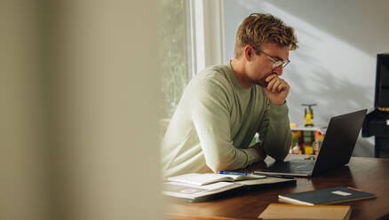 Man sitting at table and looking laptop with hand on chin. Man working on laptop and thinking. - JLPSF08213