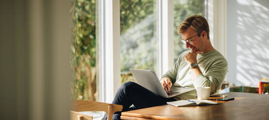 Young man using laptop and smiling at home. Man sitting by table working on laptop computer. - JLPSF08222