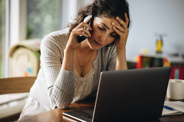 Woman holding her head and talking on mobile phone. Stressed woman making a phone call while working from home. - JLPSF08229