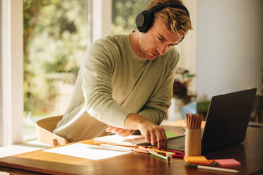 Man wearing headphones working on his illustrations at home. Male illustration artist sitting at table with laptop. - JLPSF08236