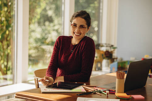 Porträt einer lächelnden Designerin, die zu Hause sitzt und mit einem digitalen Tablet an einer Illustration arbeitet. - JLPSF08244
