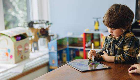 Niedlicher Junge, der mit einem Stift auf einem Grafiktablett zeichnet. Ein Kind benutzt ein digitales Tablet und einen Stift. - JLPSF08247