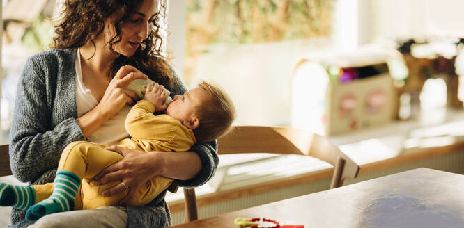 Mother feeding her newborn baby with bottle at home. Infant baby lying on mothers hand drinking milk from bottle. - JLPSF08252