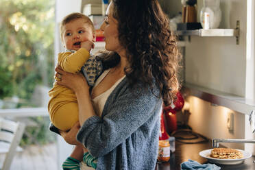 Eine Frau im Mutterschaftsurlaub verbringt Zeit mit ihrem Baby. Eine Mutter, die ihr Baby trägt, steht in der Küche. - JLPSF08258