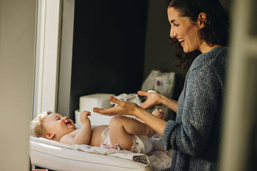 Frau spielt mit ihrem Baby, während sie seine Kleidung wechselt. Frau verbringt Zeit mit ihrem Baby, während sie im Mutterschaftsurlaub ist. - JLPSF08266