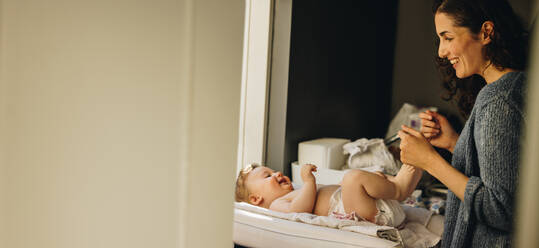 Loving mother talking with her baby lying on changing table. Woman changing clothes of baby at home. - JLPSF08267