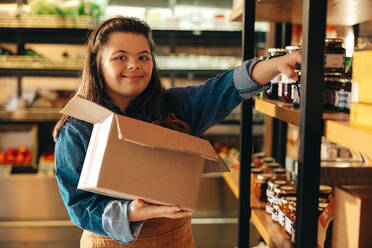 Convenience store employee with Down syndrome restocking food products onto the shop shelves. Empowered woman with an intellectual disability working as a shopkeeper in a grocery store. - JLPSF08289