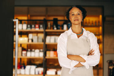 Confident small business owner looking at the camera while standing at the entrance of her grocery store with her arms crossed. Mature entrepreneur running a trendy convenience store. - JLPSF08297