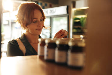Fröhliche junge Frau, die das Etikett eines Lebensmittels in der Lebensmittelabteilung eines Lebensmittelladens liest. Fröhliche junge Frau beim Einkaufen in einem trendigen Supermarkt. - JLPSF08307