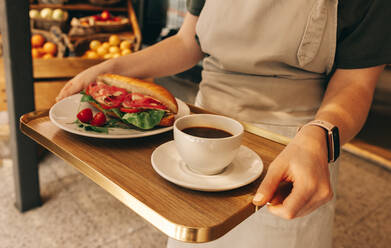 Unbekannte junge Kellnerin, die ein Tablett mit einem Sandwich und einer Tasse Kaffee trägt. Junge Frau, die als Bedienung in einem Schnellrestaurant arbeitet. - JLPSF08316