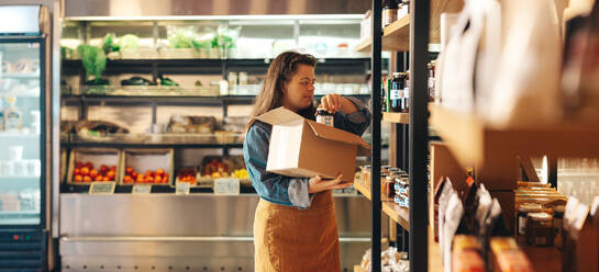 Mitarbeiterin mit Down-Syndrom beim Auffüllen der Lebensmittelvorräte in einem Lebensmittelgeschäft. Selbständige Frau mit geistiger Behinderung, die als Verkäuferin in einem örtlichen Supermarkt arbeitet. - JLPSF08323