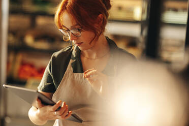 Ladenbesitzerin bei der Inventur mit einem digitalen Tablet in ihrem Lebensmittelgeschäft. Junge Unternehmerin, die ihr kleines Unternehmen mit Hilfe von Drahtlostechnologie führt. - JLPSF08345