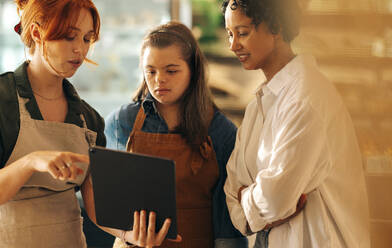 Die Leiterin eines Supermarkts nutzt ein digitales Tablet, während sie mit ihren Angestellten eine Besprechung abhält. Eine Gruppe verschiedener Frauen arbeitet in einem kleinen Unternehmen zusammen, das ausschließlich von Frauen geführt wird. - JLPSF08354