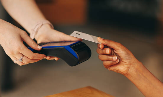 Eine Café-Kundin scannt ihre Kreditkarte auf einem Kartenautomaten, um ihre Rechnung zu bezahlen. Eine nicht erkennbare Frau führt eine bargeldlose und kontaktlose Transaktion mit NFC-Technologie durch. - JLPSF08360