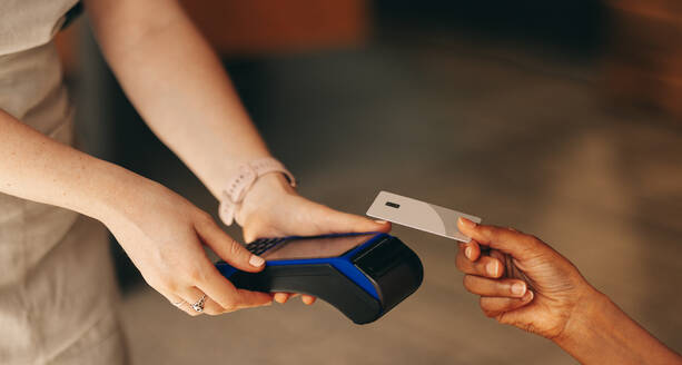 Unbekannte Kundin scannt ihre Kreditkarte auf einem Kartenautomaten, um ihre Rechnung in einem Café zu bezahlen. Frau bei einer bargeldlosen und kontaktlosen Transaktion mit NFC-Technologie. - JLPSF08361