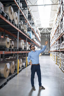Businessman wearing virtual reality simulator gesturing in aisle at factory - JOSEF14414