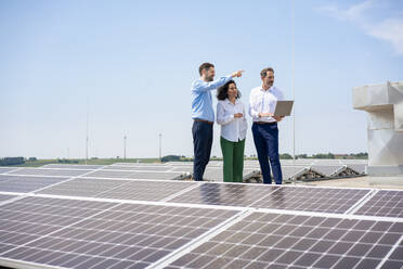 Geschäftsmann gestikuliert vor Kollegen, die über Sonnenkollektoren auf dem Dach diskutieren - JOSEF14434