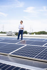Businessman standing by solar panels on rooftop - JOSEF14454