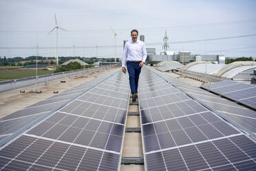 Smiling businessman walking amidst solar panels on rooftop - JOSEF14459