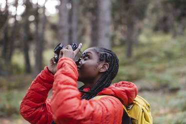 Junge Frau mit geflochtenem Haar beim Fotografieren im Wald - JCCMF07434