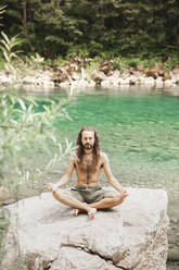 Hemdloser junger Hipster meditiert im Lotussitz auf einem Felsen - PCLF00178
