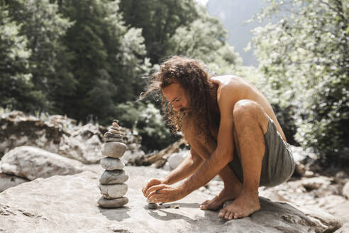 Mann ohne Hemd hockt auf einem Felsen und stapelt Steine - PCLF00179